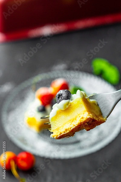 Fototapeta A blueberry on a piece of tasty lemon curd tart with whipped cream and fresh berries on the top. Close up. Vertical orientation.