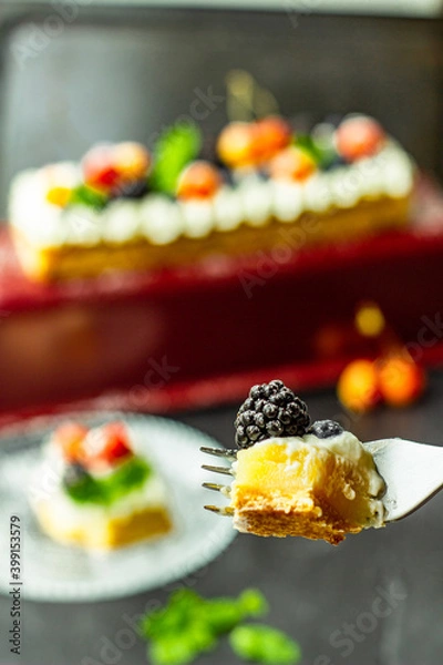 Fototapeta A sugar powdered blackberry on a piece of tasty lemon curd tart with whipped cream and fresh berries on the top. Close up. Vertical orientation.