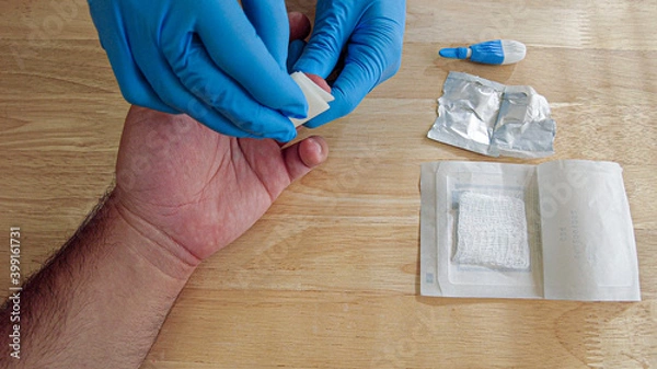 Fototapeta A medical personnel wearing gloves is wiping the finger tip of a patient with a sterile alcohol wipe before performing a finger prick blood draw for a diagnostic test at a doctor's office