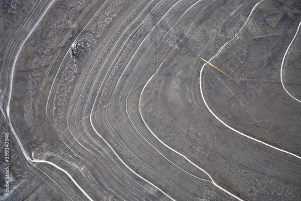 Fototapeta Frozen puddle - abstract circular lines shape this thin layer of frozen ice on a shallow muddy puddle.