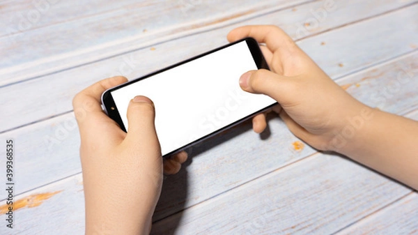 Fototapeta 
The child is holding a phone with a white screen at the table. Child's phone with white screen
