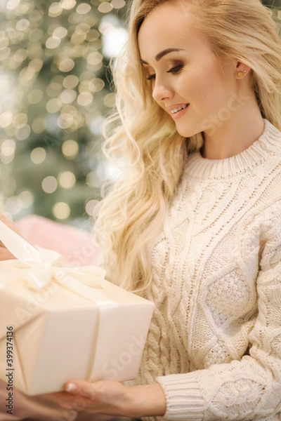 Fototapeta Portrait of Beautiful blond hair woman in pullover open present on Chrisrmas time. Elegant woman by Christmas tree. Attractive female hold present. Christmas mood