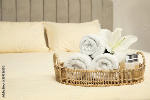 Fototapeta Rolled clean towels and shampoo bottles on bed. Space for text