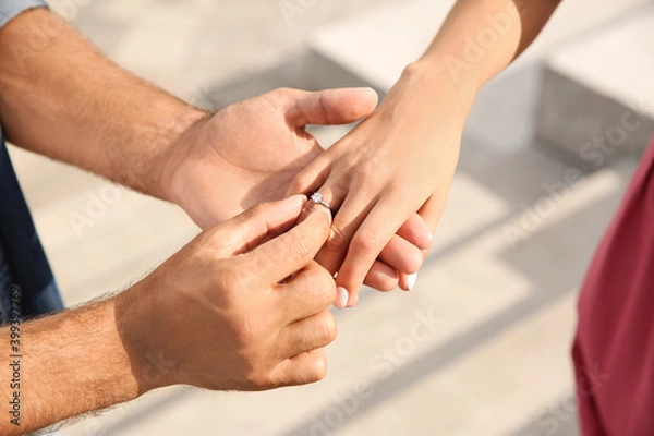 Fototapeta Man putting engagement ring on his girlfriend's finger outdoors, closeup