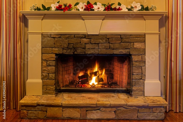 Fototapeta Glowing fire in a stone fireplace decorated with red and white flowers.