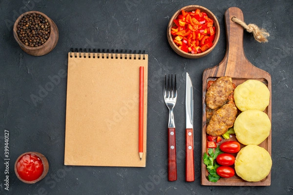 Fototapeta Top view of tasty cutlets chopped vegetables greens for dinner and notebook on dark background