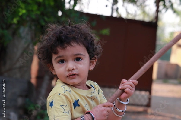 Fototapeta A little child looking at the camera holding a wooden stick