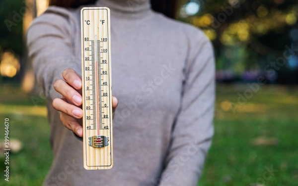 Fototapeta Closeup image of a woman holding and showing thermometer in the outdoors