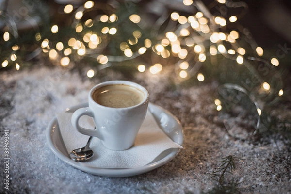 Fototapeta A cup of espresso surrounded by New Year's lights and pine branches in the snow. Dark background. Christmas mood