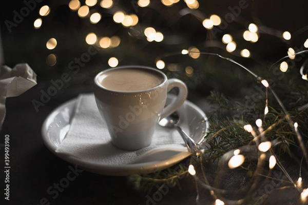 Fototapeta Espresso surrounded by New Year's lights and pine branches. Food dark background. Christmas lunch in a cafe
