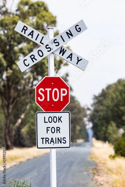 Fototapeta Red stop sign at a railway crossing on a country road running to the horizon. Outback Australia.