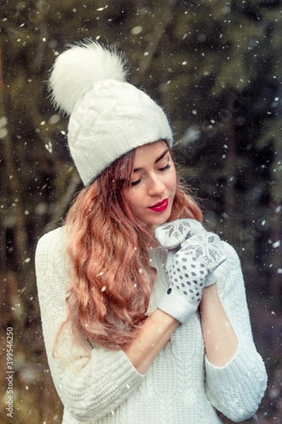 Fototapeta A girl in a white hat and warblers is warming up, it is snowing. winter.