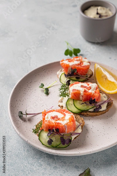 Fototapeta Mini open sandwiches with smoked salmon, cream cheese, cucumber and microgreen on rye bread, grey stone background. Appetizer with salmon and cheese cream sauce.