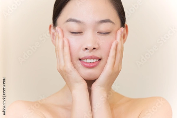 Fototapeta 美容フェイシャルイメージ　両手にひらで頬を包む若く美しいアジア女性