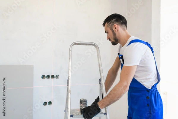 Fototapeta A bearded builder moves an aluminum step ladder around the room