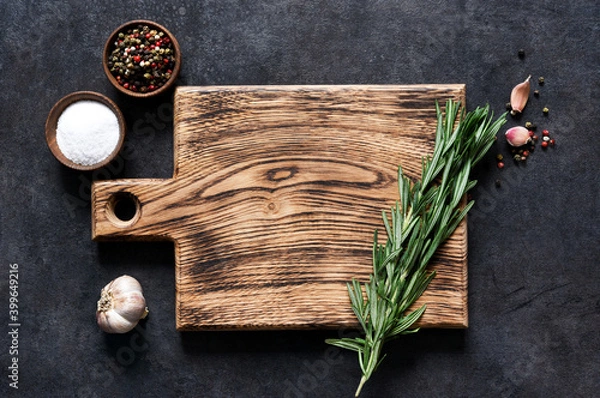 Fototapeta Cutting board with fresh rosemary and spices on a black concrete table. Top view with copy space