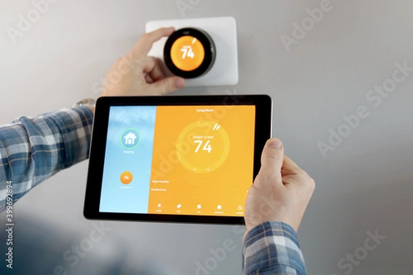 Fototapeta Man is Adjusting a temperature using a tablet with smart home app in modern living room