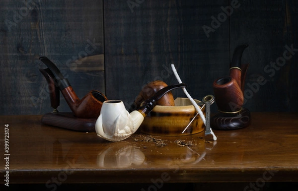 Fototapeta Composition with smoking pipes: in the foreground a pipe made of sea foam (meerschaum), two of heather and one of cherry, an ashtray, pipe cleaning accessories and tobacco crumbs.