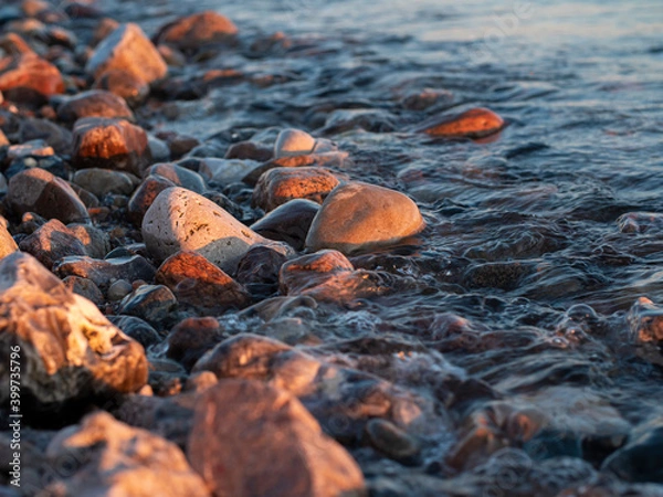 Fototapeta Rocks and pebbles on the beach being watered as the waves wash in on the beach at sunset