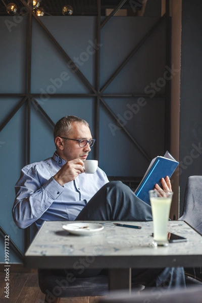 Fototapeta Businessman drinking coffee and reading plans in a cafe.