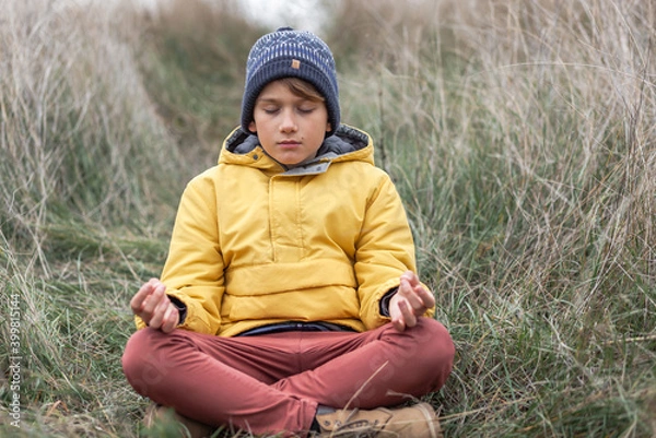 Fototapeta Little boy exercising Yoga in Lotus position during autumn day in a meadow.