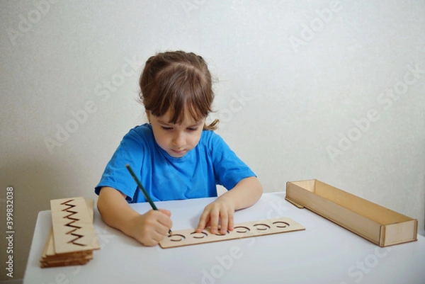 Fototapeta Insert templates for preparing the preschooler's hands for writing. Early development concept. The girl is learning to write.