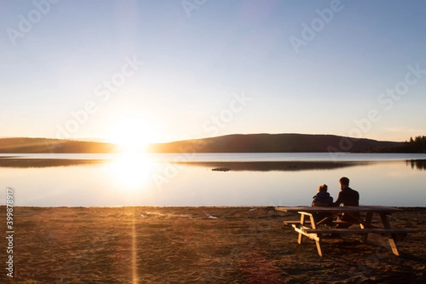 Obraz Couple sitting at a picnic table and admiring the sunset over the lake Touladi in the Temiscouata national park, Canada
