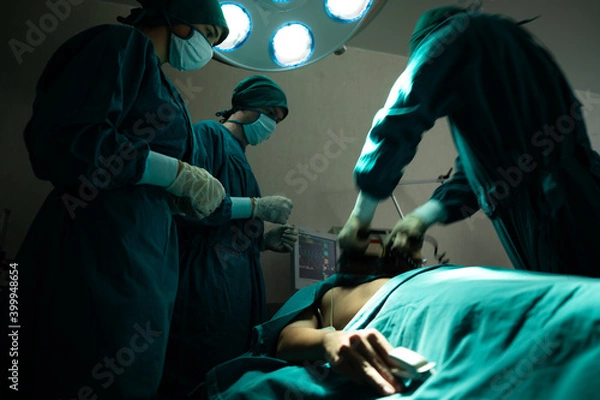 Fototapeta professional surgery team in the operating room, urgent surgery. Professional smart intelligent surgeons standing near the patient and performing an operation while saving his life