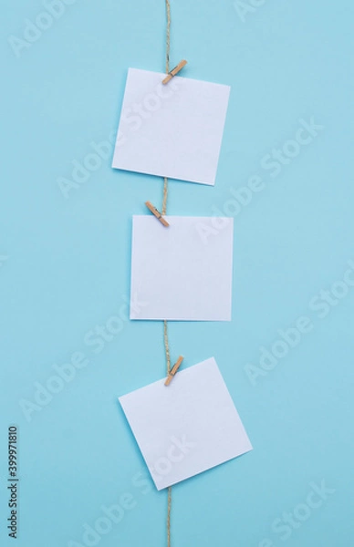Fototapeta three blank note papers attached to a rope on vertical blue background