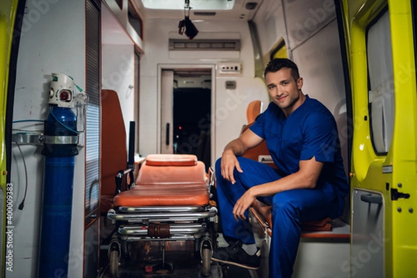Fototapeta Smiling paramedic in a blue uniform sitting in the back of an ambulance car.
