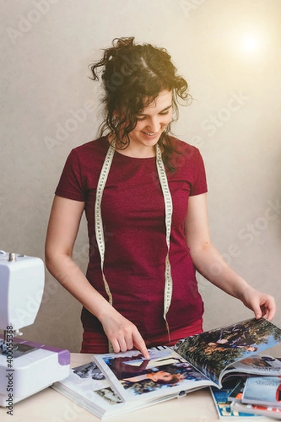 Obraz Happy attractive young woman seamstress sitting and sews on sewing machine in studio