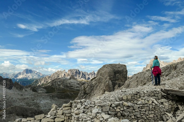 Obraz A woman hiking in high and desolated mountains in Italian Dolomites. She stands at the edge of a slope and enjoys the idyllic landscape. Raw and unspoiled landscape. Sunny day. Endless mountain chains