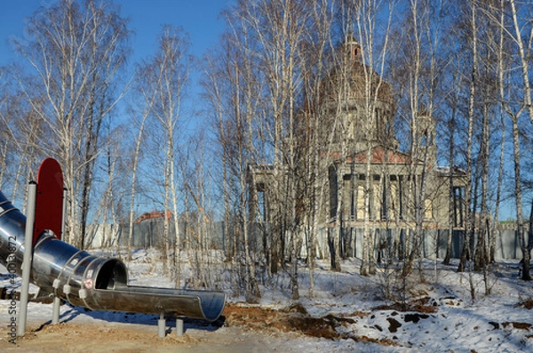 Fototapeta Children's play construction against the backdrop of an Orthodox Cathedral under construction in Chelyabinsk, Russia.