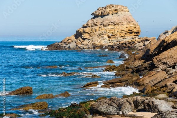 Fototapeta Sea waves breaking on a rocks. Deep blue sea waves hit cliff, hit rocks cliff. Mighty sea waves breaking on a cliff, splashing over rocks. Strong ocean waves hitting rocks