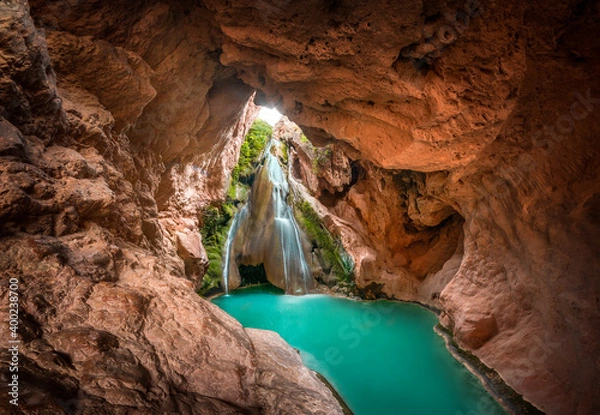 Fototapeta A beautiful waterfall inside a cave and a lake of crystal clear turquoise water. Enchanted landscape, a cave inside a mountain in which there is a waterfall and a crystalline river. Bercolon waterfall