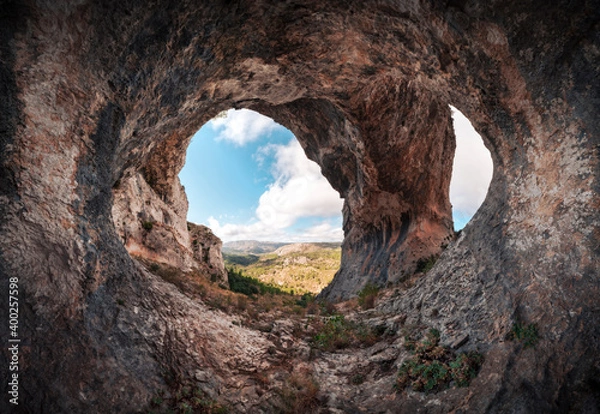 Fototapeta Panoramic of a large cave with two entrances. Interior of a cavern with a stone arch at the entrance. Cueva de los Arcos, Spain. Ancient ancestral cave in the mountain shows us a beautiful landscape