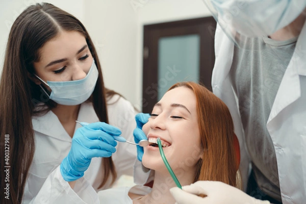 Fototapeta Gloved technicians examine a smiling client's teeth using a dental mirror