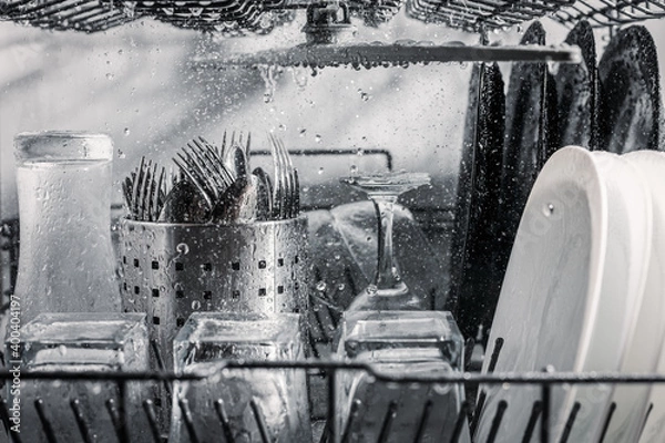 Fototapeta Transparent and black and white dishes as well as cutlery and glasses are washed in the dishwasher, inside view, drops and splashes of water.