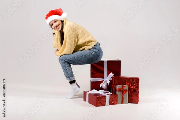 Fototapeta Woman sitting on the stack of gift christmas boxes isolated on gray background