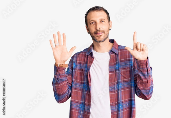 Obraz Young handsome man wearing casual clothes showing and pointing up with fingers number seven while smiling confident and happy.