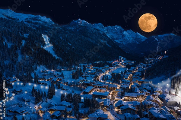 Fototapeta Night aerial view of Madonna di Campiglio city, Italy on Christmas night. Alpine town in the snow. Large yellow moon in the starry sky in the Alps. Ski town at night lights.