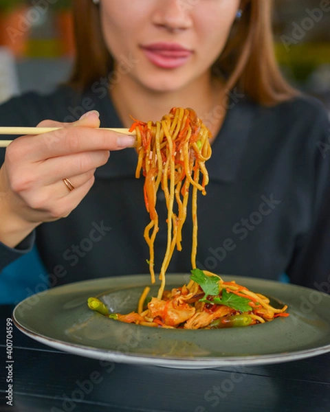Fototapeta Beautiful young woman eating chinese food called Wok with chopsticks. Wok with meat and fried asparagus in a plate.