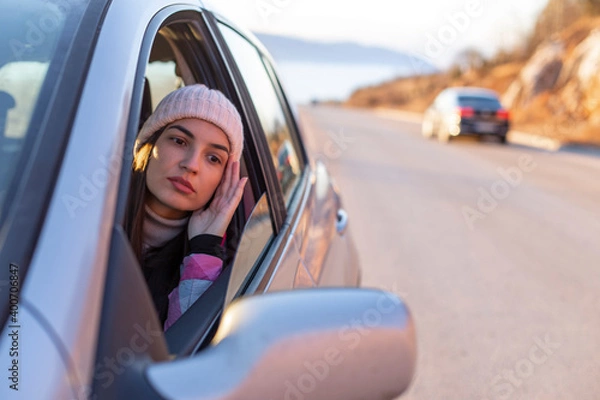 Fototapeta A woman with a winter hat is driving on a mountain and looking in the rearview mirror.
