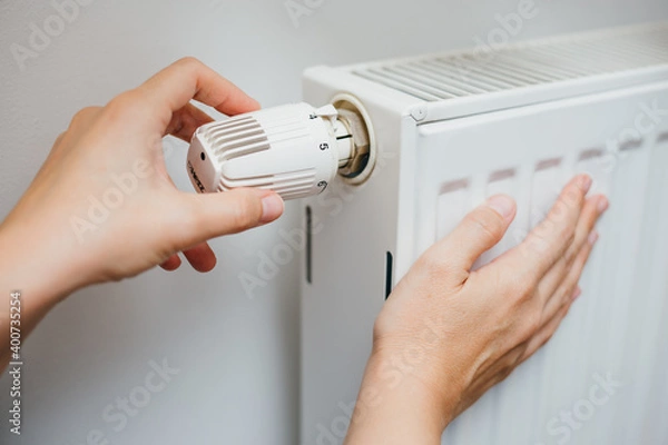 Fototapeta Close up shot of Caucasian female's hand adjusting radiator temperature using thermostat. Home with central heating.