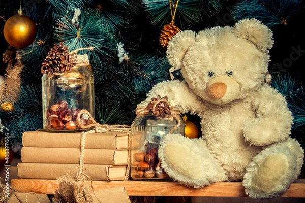 Obraz Close up beige teddy bear under christmas tree. Christmas decoration with vintage toys, golden balls, books in craft wrapper, glass jar with pine cones. vintage toning. Present for child on New Year