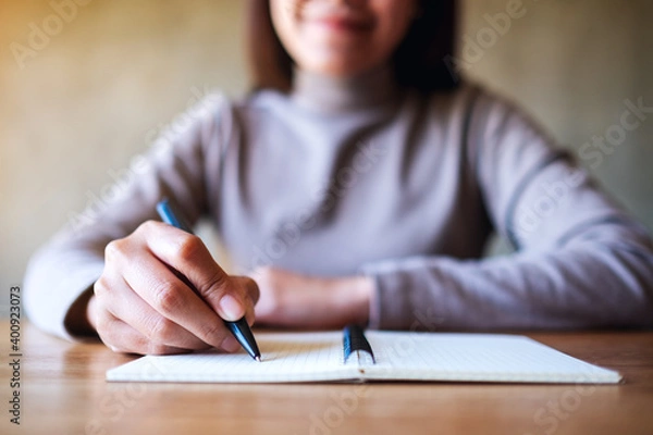Fototapeta Closeup image of a woman writing on a blank notebook on the table