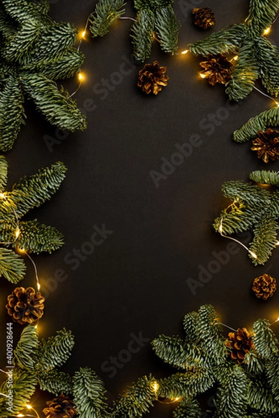 Fototapeta garland of fir branches and cones and lights on a black background with copy space