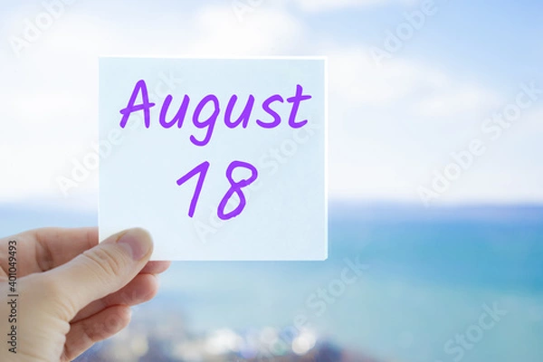 Fototapeta August 18th. Hand holding sticker with text August 15 on the blurred background of the sea and sky. Copy space for text. Month in calendar concept
