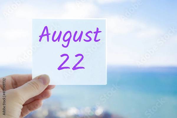 Fototapeta August 22nd. Hand holding sticker with text August 15 on the blurred background of the sea and sky. Copy space for text. Month in calendar concept