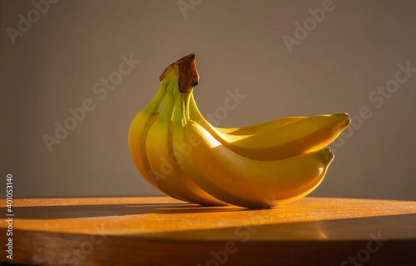 Fototapeta Still life of bananas. Bunch of bananas on a wooden table lit by natural sunlight. Minimal creative design. Dark background,
